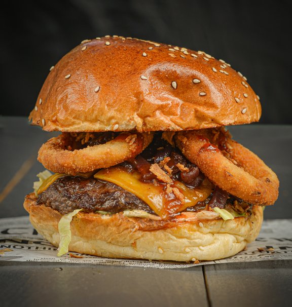 Az SD Witch Ínyenc burgere, összetevői: Kiscipó buci, hamburgerszósz, friss saláta, 100% marhahúspogácsa, cheddar sajtszelet, hagymalekvár, pirított hagyma, sült hagymakarika, BBQ szósz